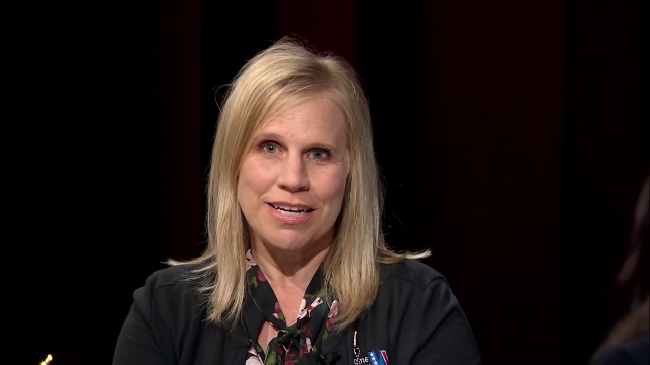 A woman in black shirt sitting down with her hands on the table.